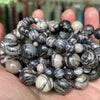 A collection of natural gemstone beads including tiger eye, lava, and turquoise stones held in a hand.