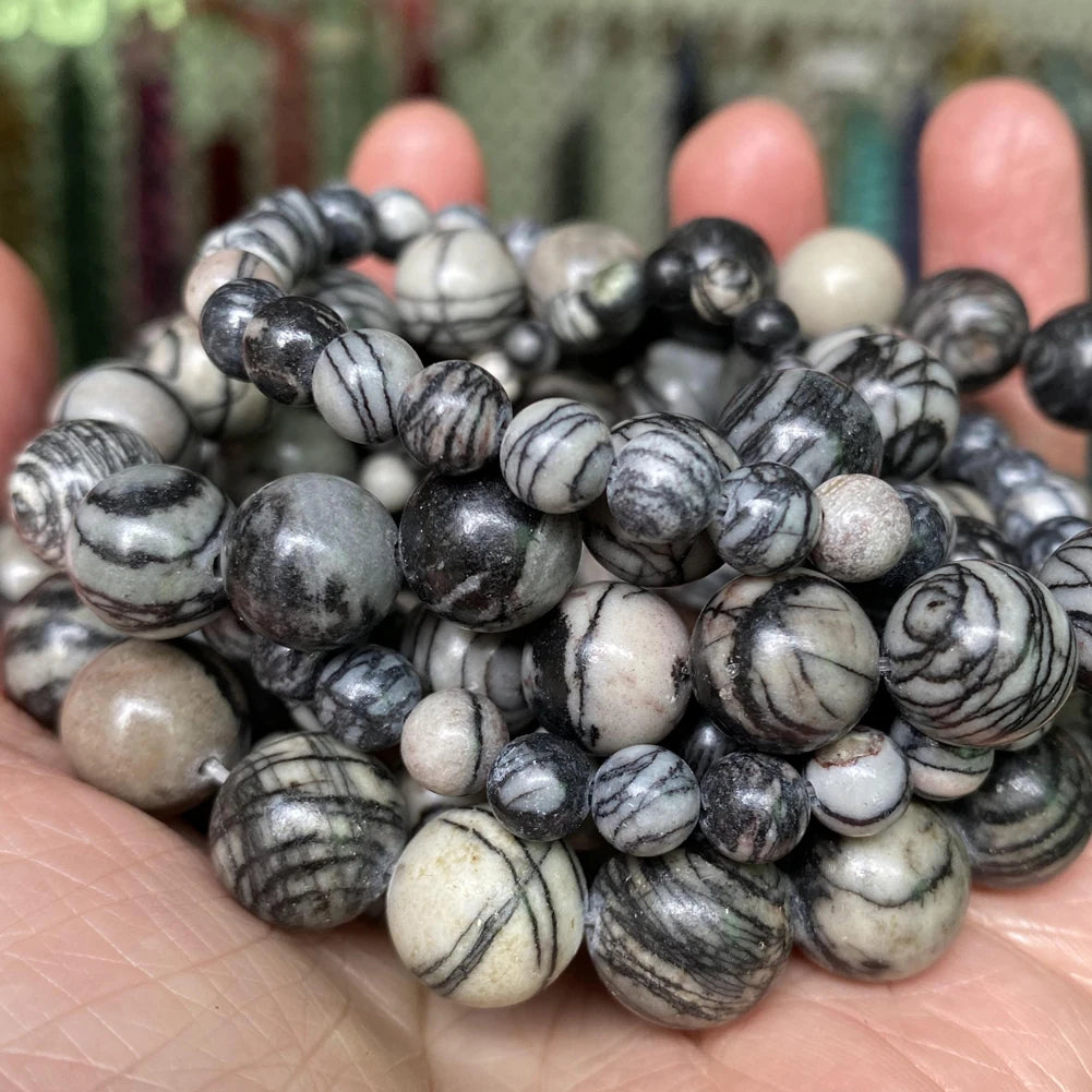 A collection of natural gemstone beads including tiger eye, lava, and turquoise stones held in a hand.