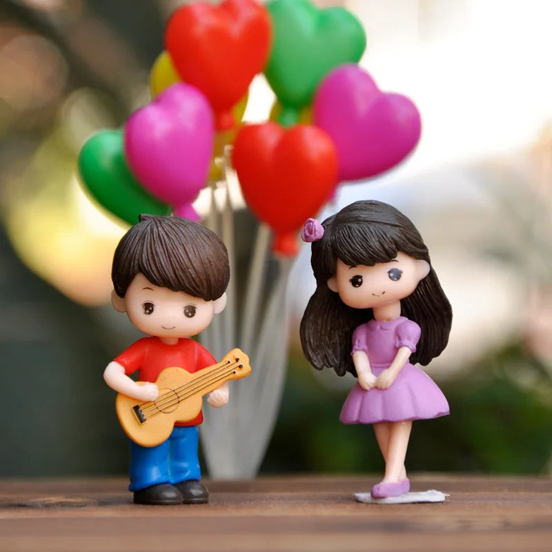 A pair of musical couple figurines, one playing a guitar and the other standing, surrounded by heart-shaped decorations.
