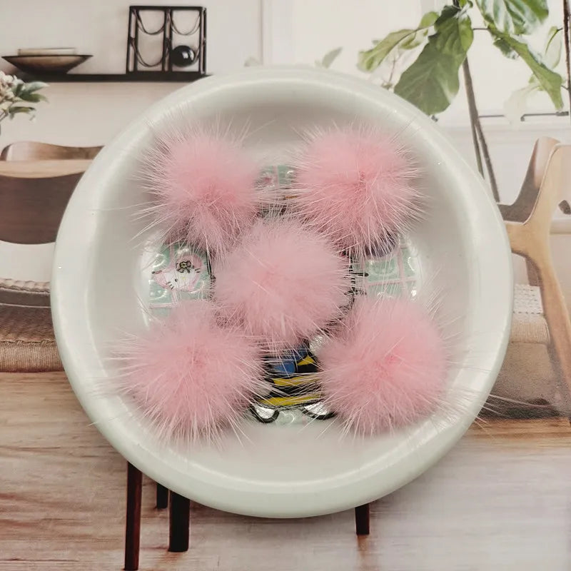 A white bowl filled with pink fluffy mink fur pom poms for crafts and accessories.