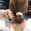 A woman's back shows elegant pearl hair ties styled into a ponytail with a bow scrunchie.