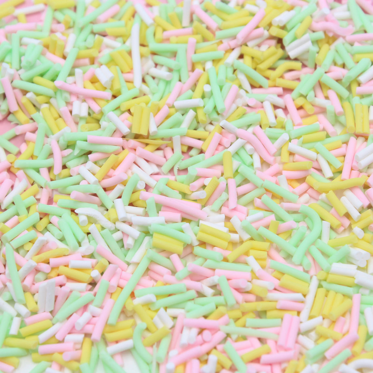 A close-up view of multicolored soft polymer clay candy sprinkles scattered on a white surface.