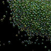 A close-up view of tiny, iridescent green and purple glass bubble beads scattered in the dark.
