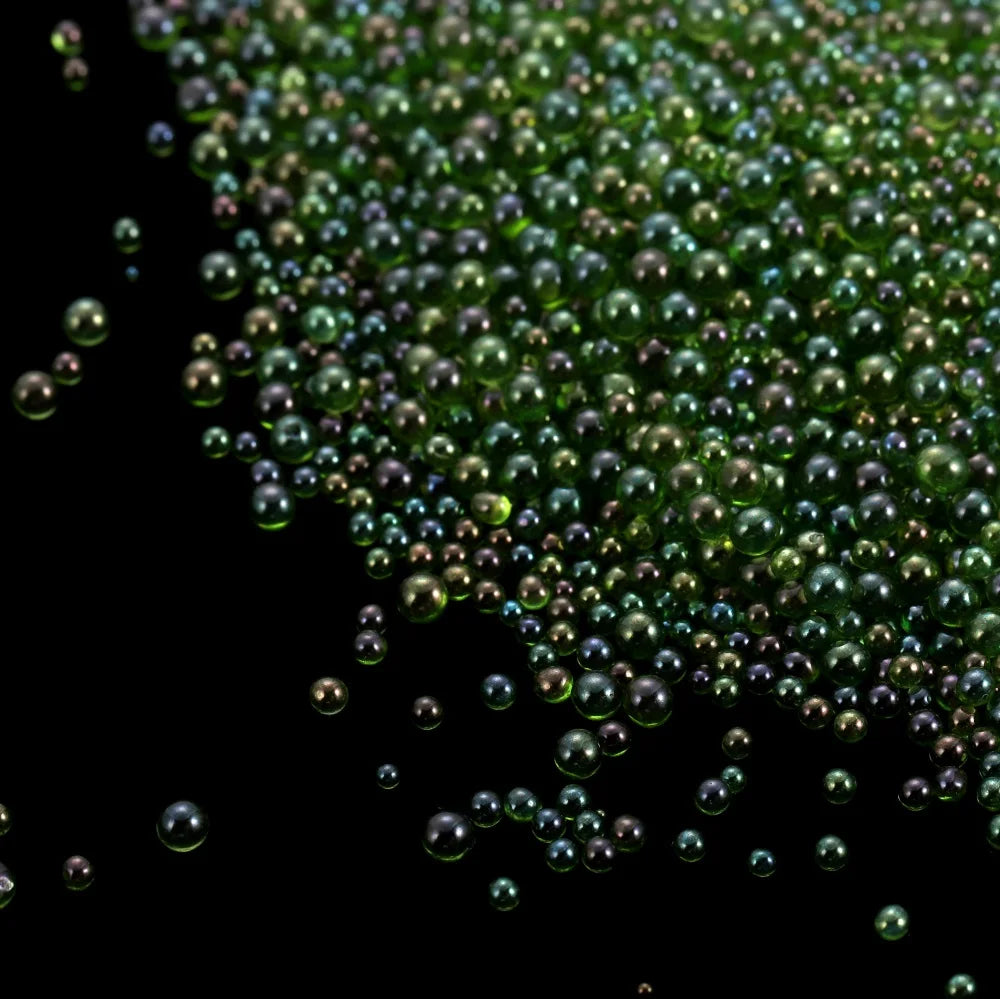 A close-up view of tiny, iridescent green and purple glass bubble beads scattered in the dark.
