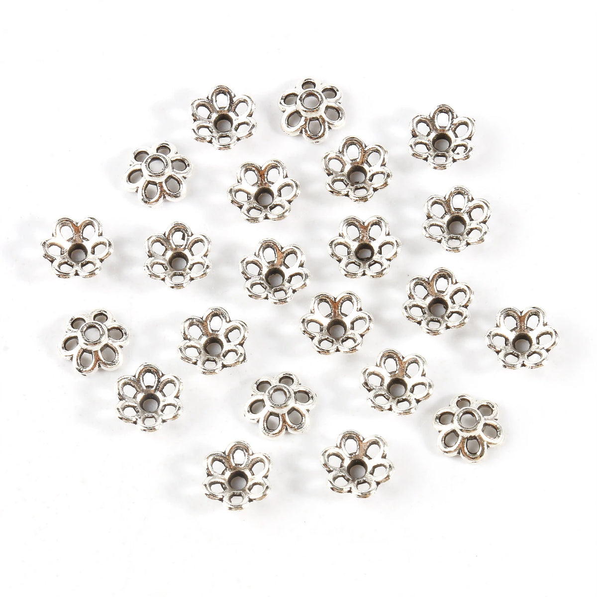 A collection of small, silver-toned Tibetan style hollow flower bead caps for jewelry making.