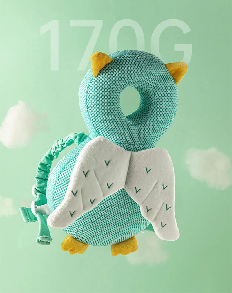 A light blue soft baby head protector pillow with yellow ears and white wings is shown against a pale green background.