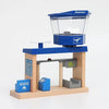 A wooden train track accessory set featuring an airport and gas station scene with blue and gray components.