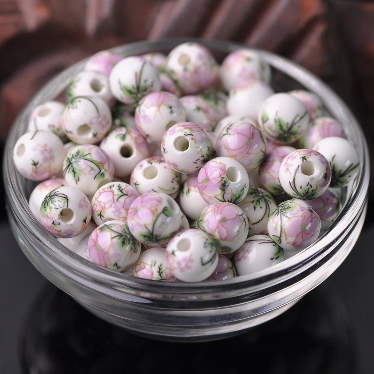 A clear glass bowl filled with small white ceramic beads decorated with pink floral patterns.