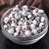 A clear glass bowl filled with white and black floral ceramic beads for jewelry making