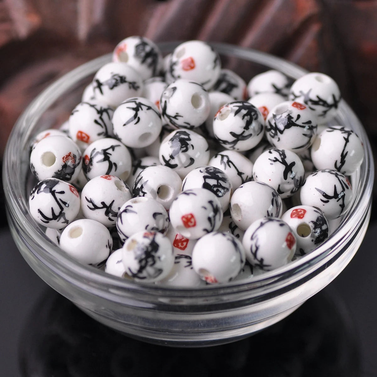 A clear glass bowl filled with white and black floral ceramic beads for jewelry making