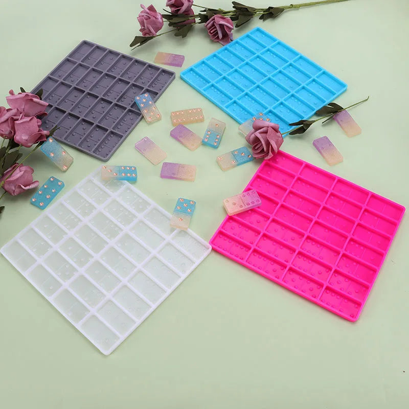 A collection of silicone mold tiles in purple, blue, and pink are arranged on a light green surface.