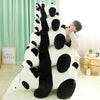 A large white and black panda plush toy is sitting on a light rug next to a window.