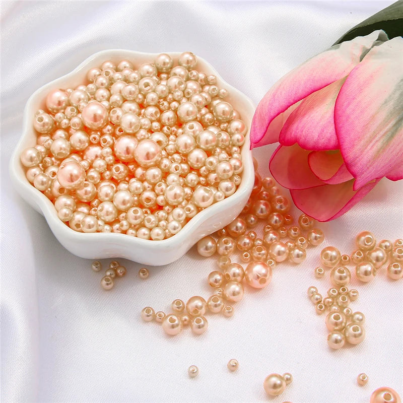 A white dish filled with assorted pink and champagne colored pearl beads next to a pink rose flower.