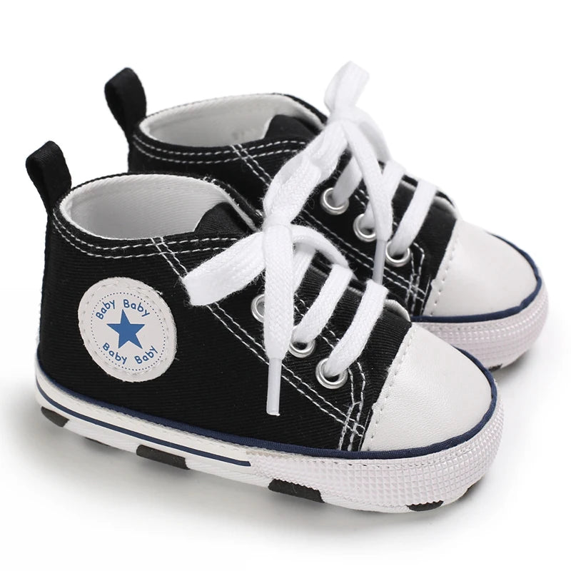 A pair of black and white canvas baby shoes with white laces and blue stitching