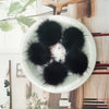 A white plate holds several fluffy black mink fur pom poms for crafts and accessories.