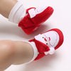 A pair of red baby winter boots with white trim and a festive design shown on a foot.