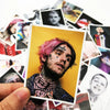 A hand holds a photo of Lil Peep with pink hair and facial tattoos, surrounded by various stickers.
