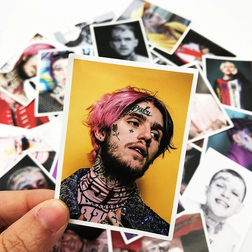 A hand holds a photo of Lil Peep with pink hair and facial tattoos, surrounded by various stickers.