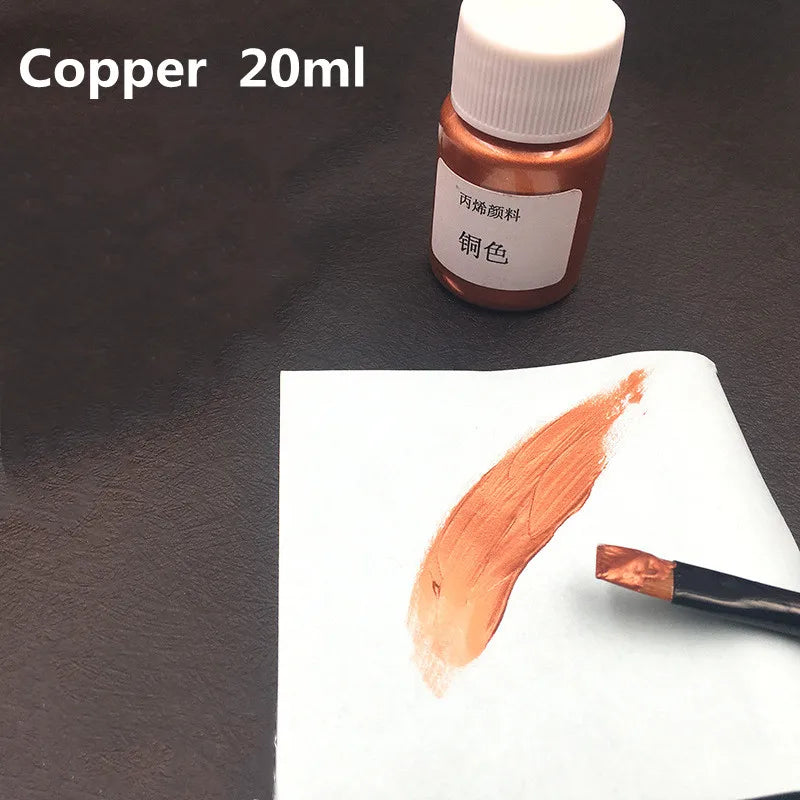 A small glass bottle of copper acrylic paint is shown next to a swatch of the metallic gold color on white paper.
