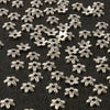 Silver Tibetan style hollow flower bead caps for jewelry making scattered on a dark surface