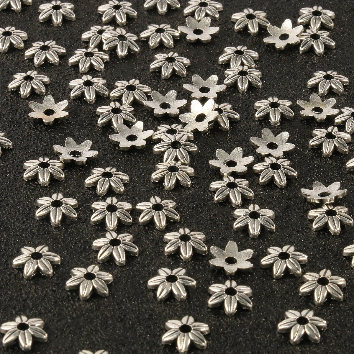 Silver Tibetan style hollow flower bead caps for jewelry making scattered on a dark surface