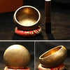 Handmade copper singing bowl with a mallet and a decorative red and gold base for meditation.