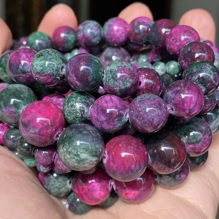 A hand holds a cluster of natural gemstone beads including tiger eye, lava, and turquoise colors.