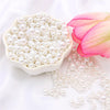 A white dish filled with assorted pearl beads and a pink lotus flower on a white background.