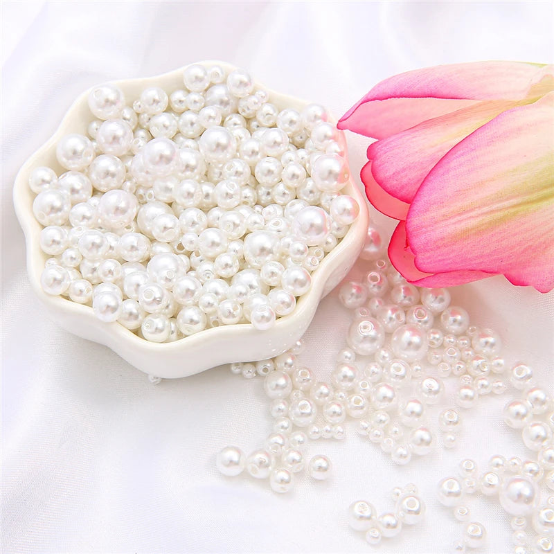 A white dish filled with assorted pearl beads and a pink lotus flower on a white background.