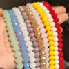 A hand holds multiple strands of faceted crystal glass beads in various pastel and vibrant colors for jewelry making