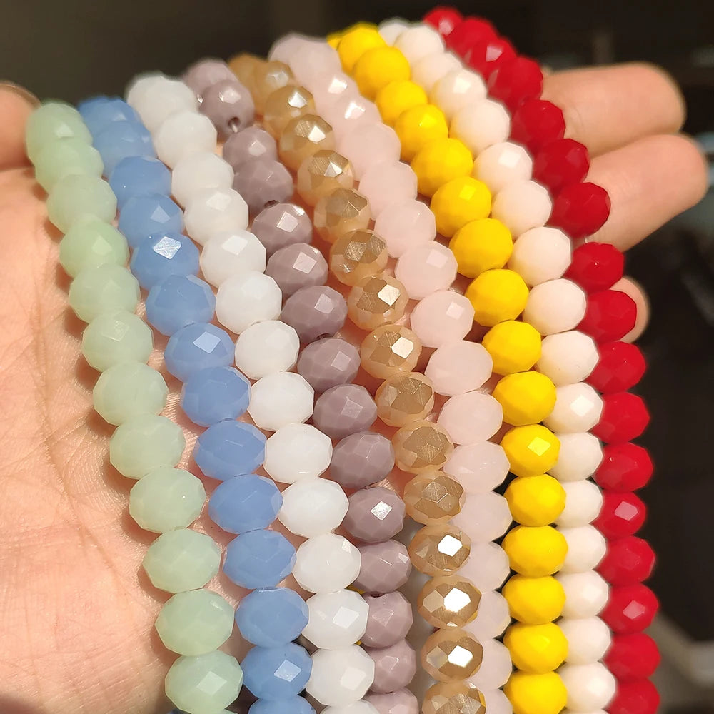 A hand holds multiple strands of faceted crystal glass beads in various pastel and vibrant colors for jewelry making