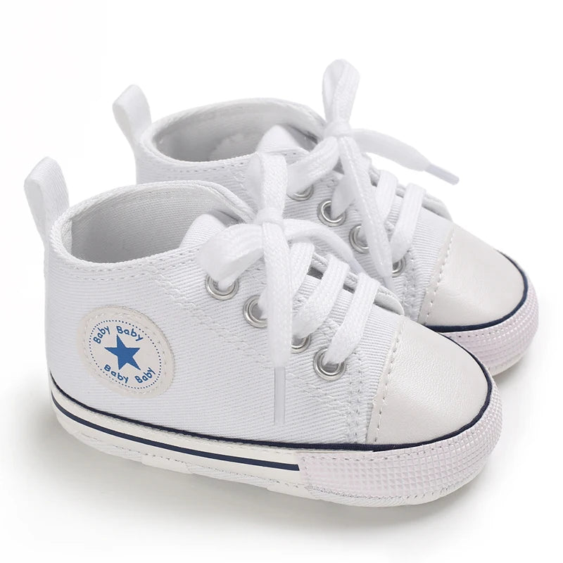 A pair of white canvas baby shoes with laces and a star embroidered on the side