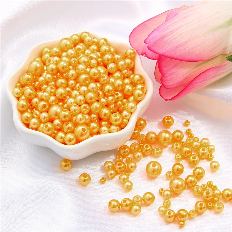 A pile of small, round, golden pearl beads is displayed next to a pink rose petal.