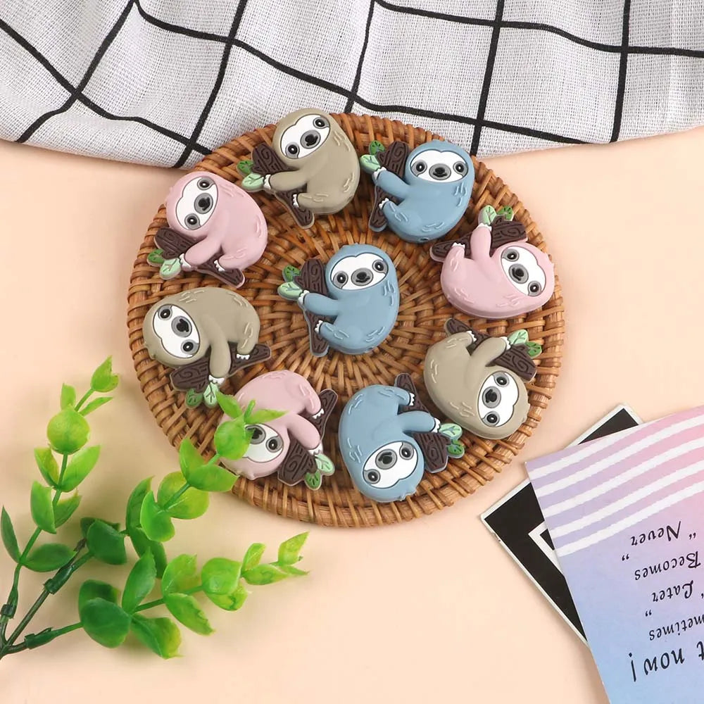A collection of adorable sloth silicone beads in various pastel colors arranged on a woven tray.