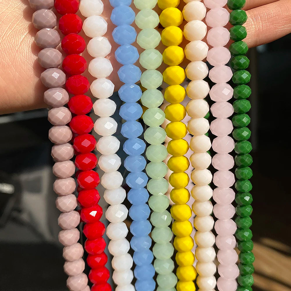 A hand holds multiple strands of faceted crystal glass beads in various colors including red, pink, white, blue, green, and y
