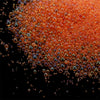 Close-up view of small, spherical orange and amber glass beads scattered on a dark surface.