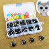 A clear plastic box contains various colorful plastic safety eyes for dolls and amigurumi, with a large cat-like face visible