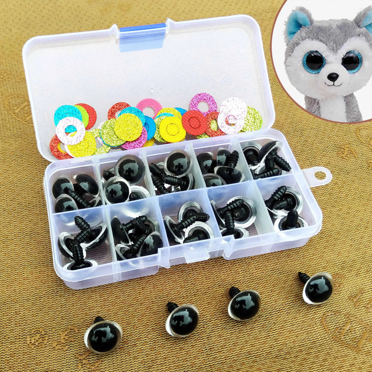 A clear plastic box contains various colorful plastic safety eyes for dolls and amigurumi, with a large cat-like face visible