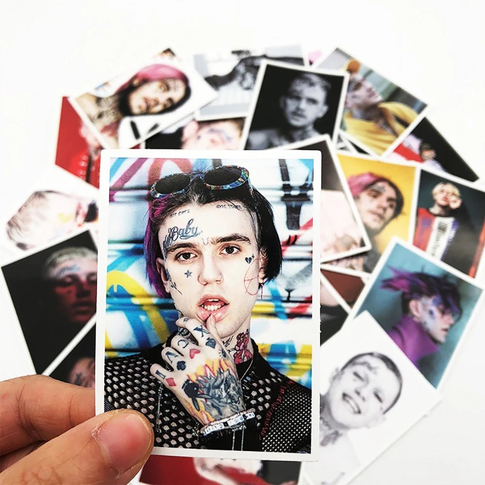 A hand holds a card featuring a portrait of Lil Peep with graffiti style markings and various stickers.