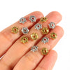 A hand holds several small, silver and gold Tibetan style hollow flower bead caps for jewelry making.