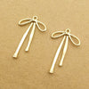 A pair of gold-colored alloy bow charms for jewelry making lying on brown paper.