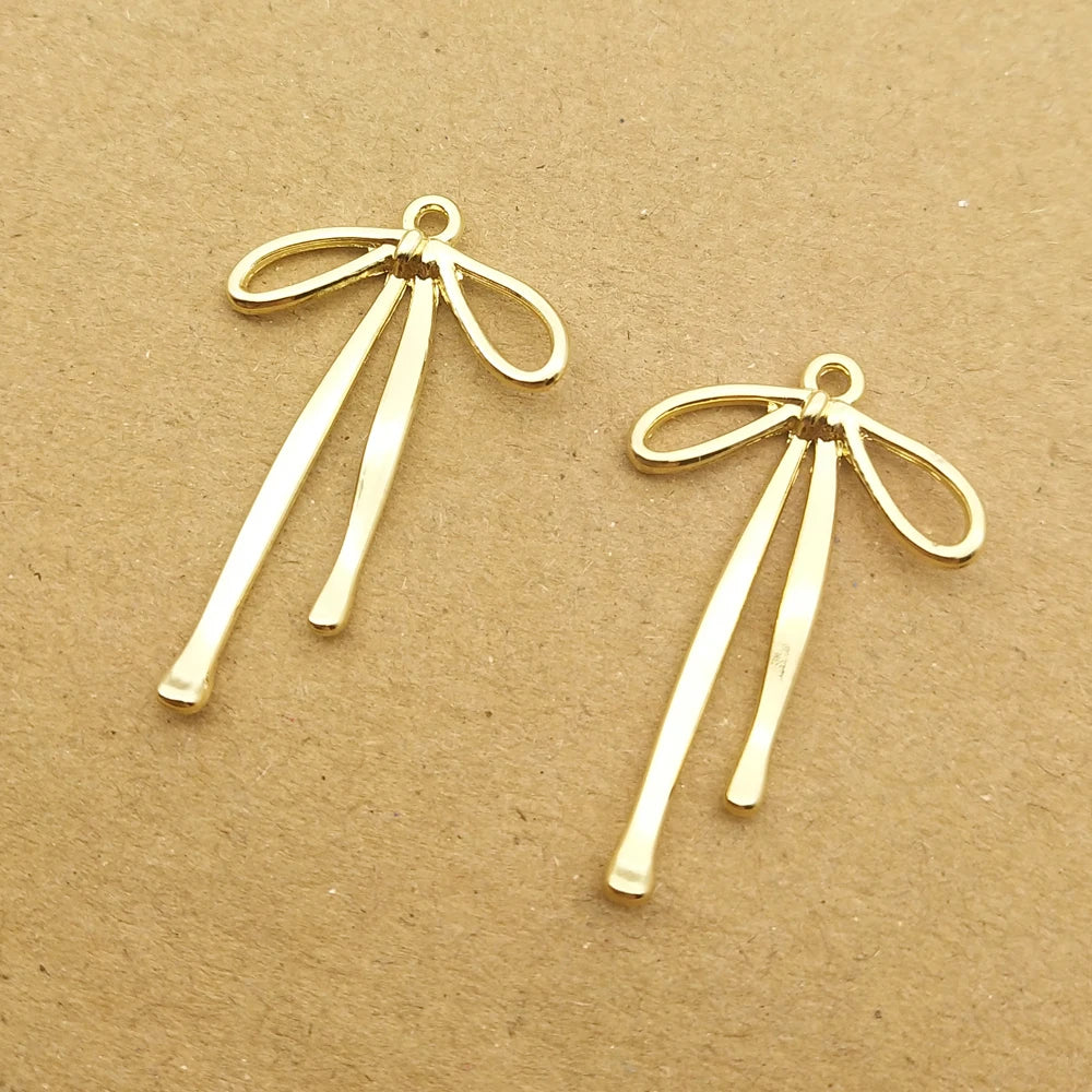 A pair of gold-colored alloy bow charms for jewelry making lying on brown paper.