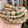 A hand holds a strand of natural gemstone beads featuring tiger eye, lava, and turquoise colors.