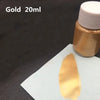 A small glass bottle of metallic gold acrylic paint with a swatch of the same gold color on a white surface.