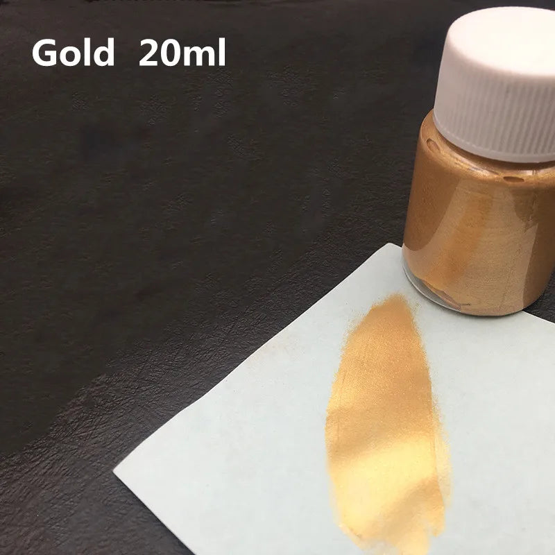 A small glass bottle of metallic gold acrylic paint with a swatch of the same gold color on a white surface.