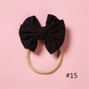 A black glitter bow headband with a light beige elastic band is displayed on a pink background.
