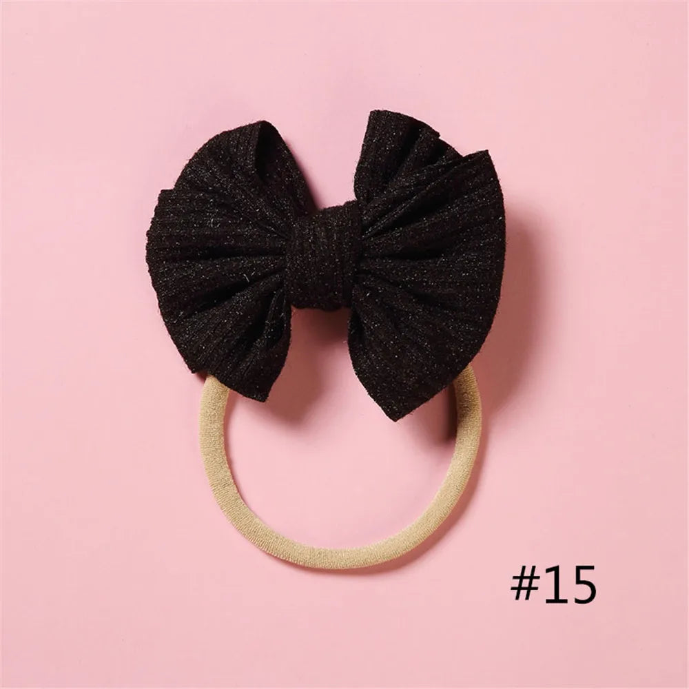 A black glitter bow headband with a light beige elastic band is displayed on a pink background.