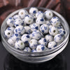 A clear glass bowl filled with small white and blue floral ceramic beads for jewelry making