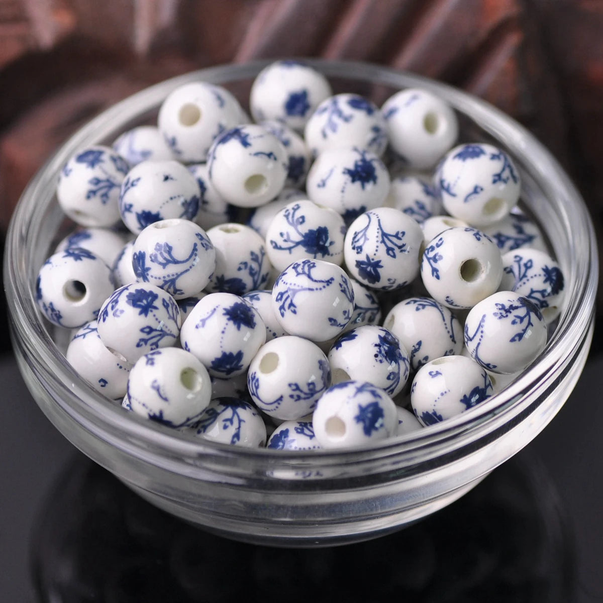 A clear glass bowl filled with small white and blue floral ceramic beads for jewelry making