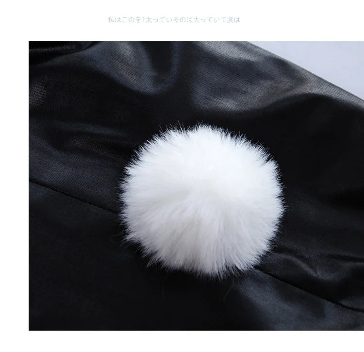 A fluffy white pom-pom decoration is placed on a piece of black faux leather fabric.